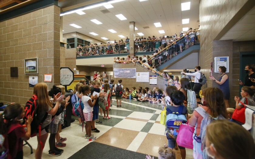 A hallway is crowded with small children who applaud as others walk through.