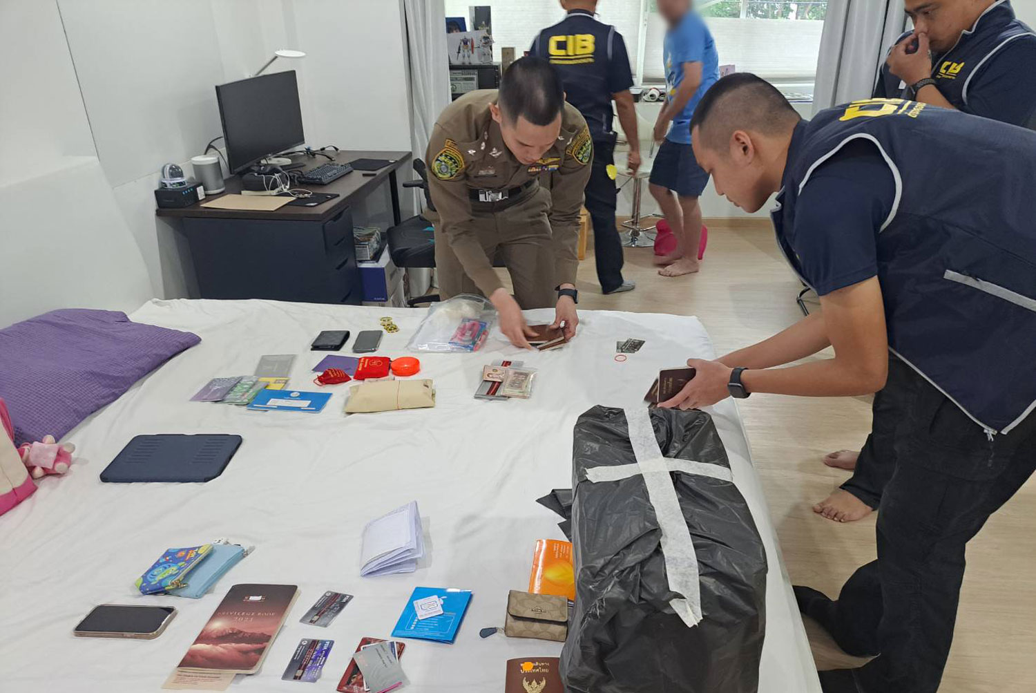 Police inspect bank passbooks and other items seized from the house of one of 10 members of an online gambling ring during raids on 12 locations in Bangkok and two nearby provinces on Wednesday. (Photo supplied/Wassayos Ngamkham)