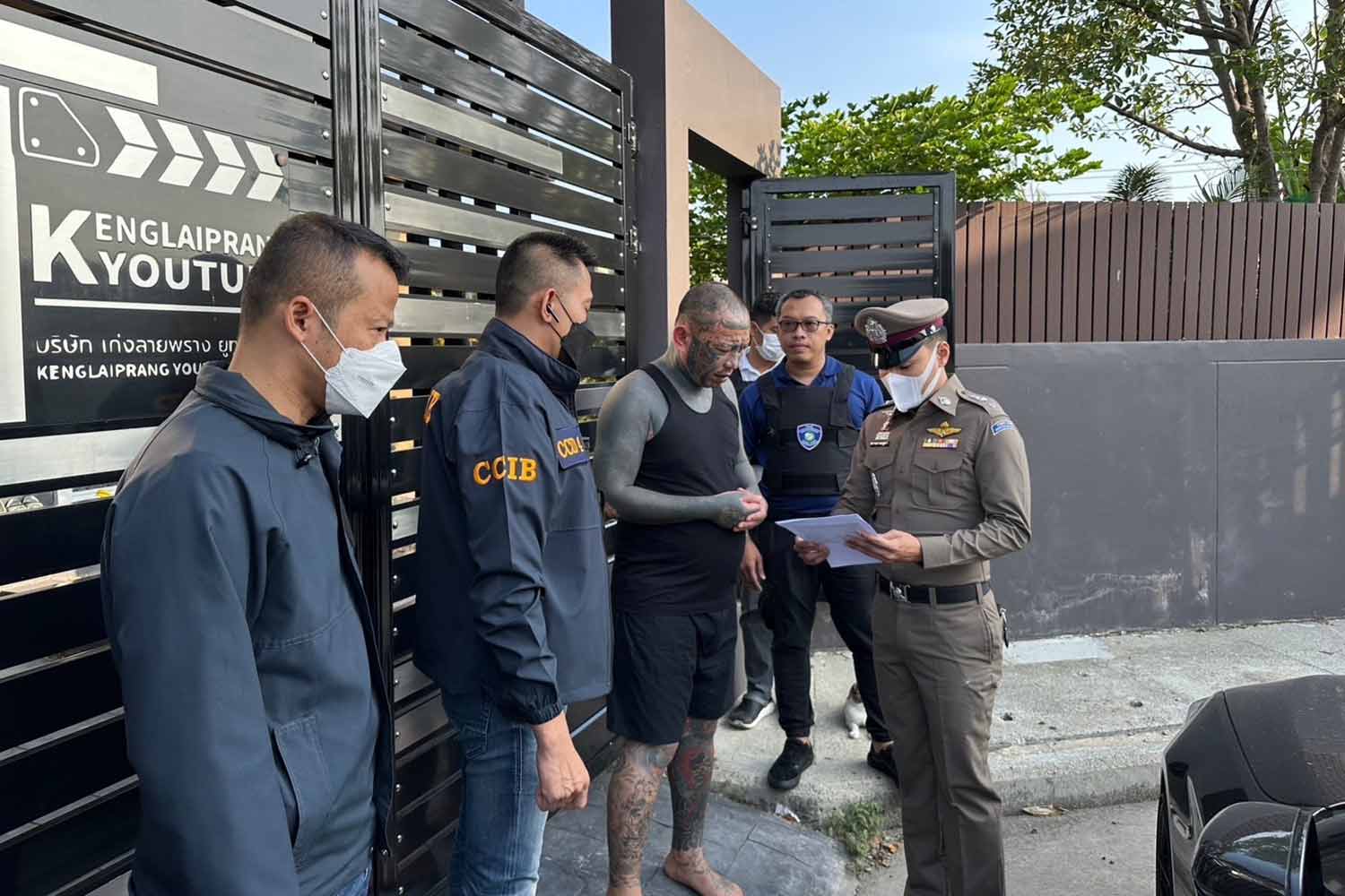 A police officer shows Jirayu Yim-ampai, alias Keng Laiprang, third from left, a court warrant to search of his office on May 7. (Police photo)