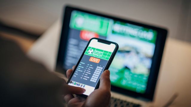 Man using mobile app for live betting and online gambling and watching a sports match