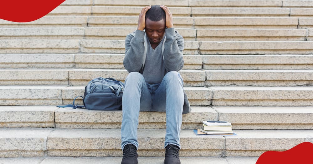 A black depressed man holding his head.