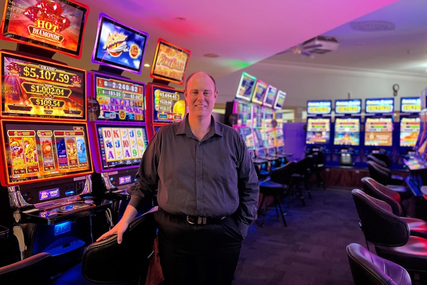 A smiling, middle-aged man in a dark shirt stands in a gaming room at a club.