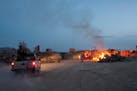 An Afghan National Army pickup truck passes parked U.S. armored military vehicles as smoke rises from a fire in a burn pit at Forward Operating Base C