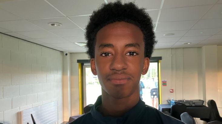 Black boy in dark-coloured top with large window in background