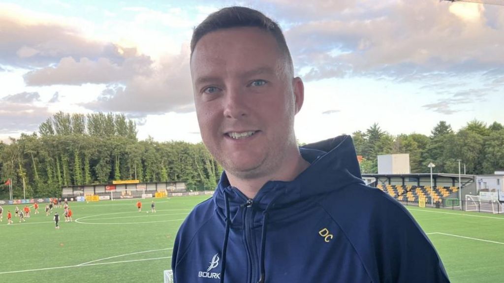 Man in navy top with football pitch in background
