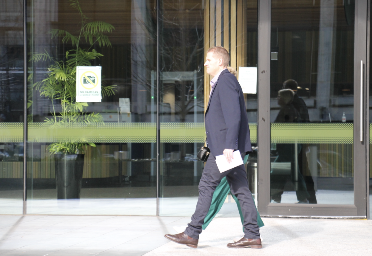 A photograph of the side profile of a man walking straight ahead