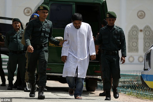 A man who is about to receive a public caning for violating Sharia law is escorted by Sharia Police in Jantho