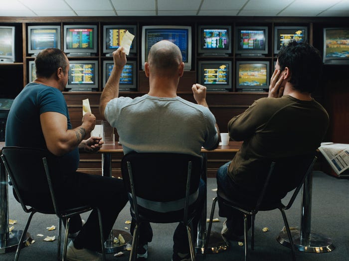 Three men sitting at a table who are gambling on sports.