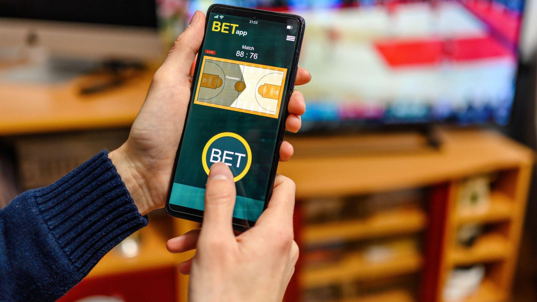 Hands holding a phone with a betting app on it.