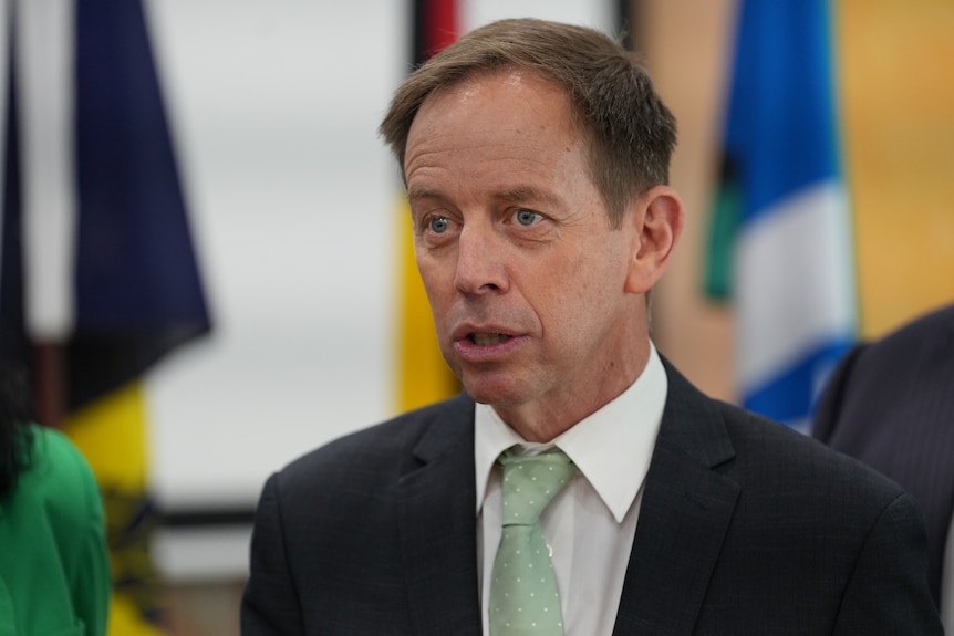 Shane Rattenbury standing in front of flags.