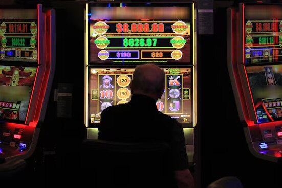 A man sitting in front of a poker machine. Two more poker machines are next to him