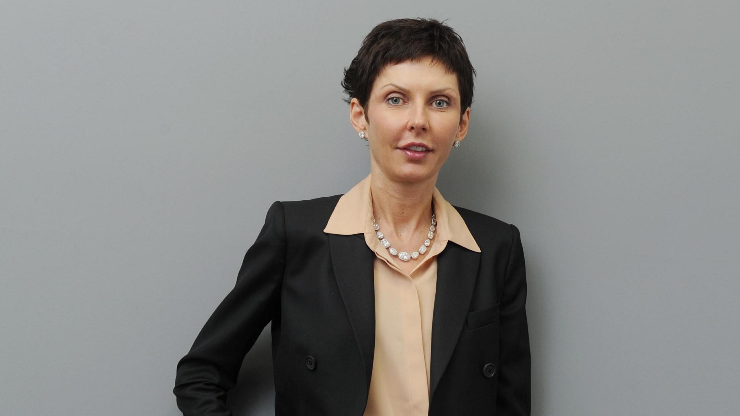 Denise Coates is pictured wearing a suit and beige shirt in a company headshot