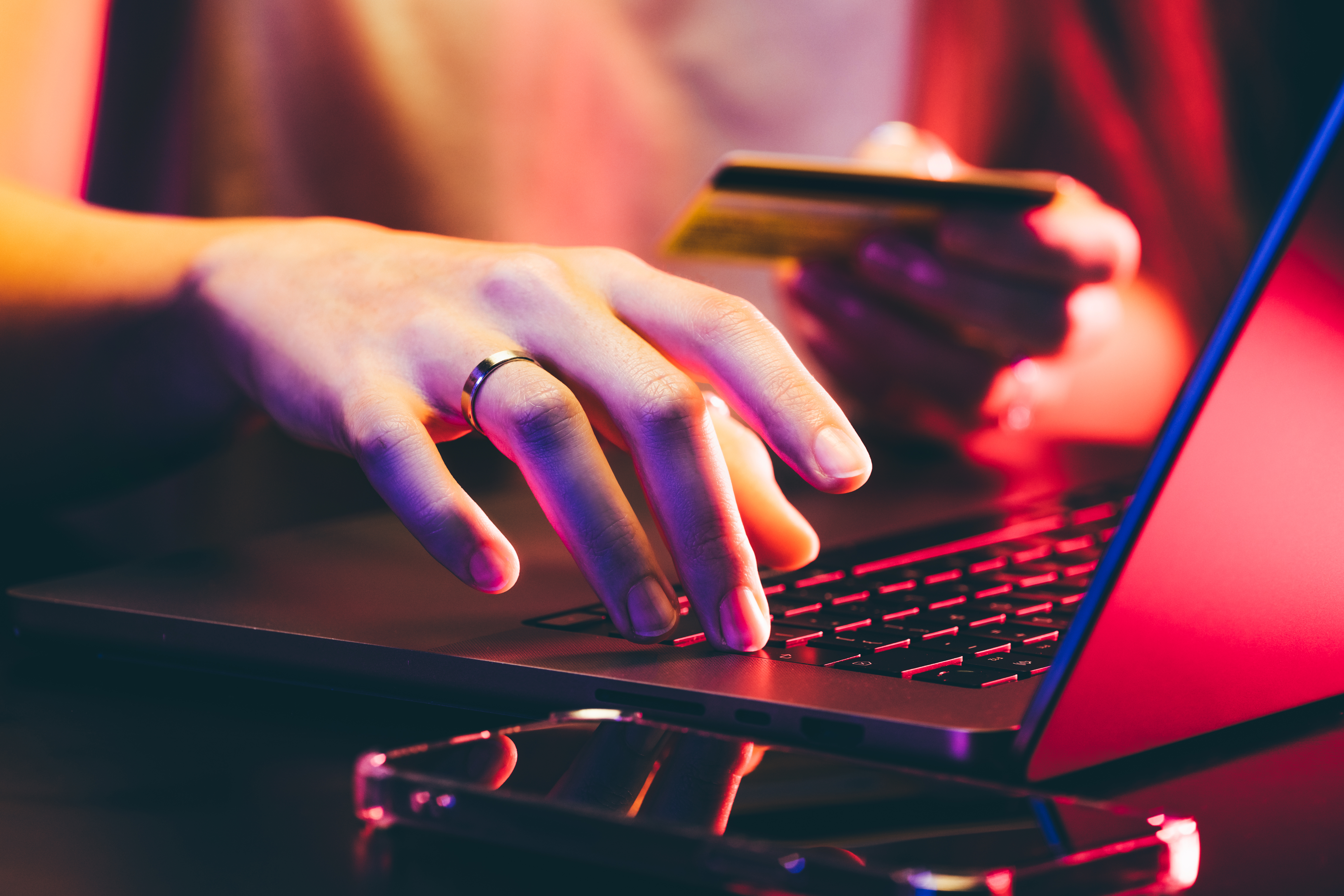 Hands holding a credit card and using a laptop under neon light. Online shopping.