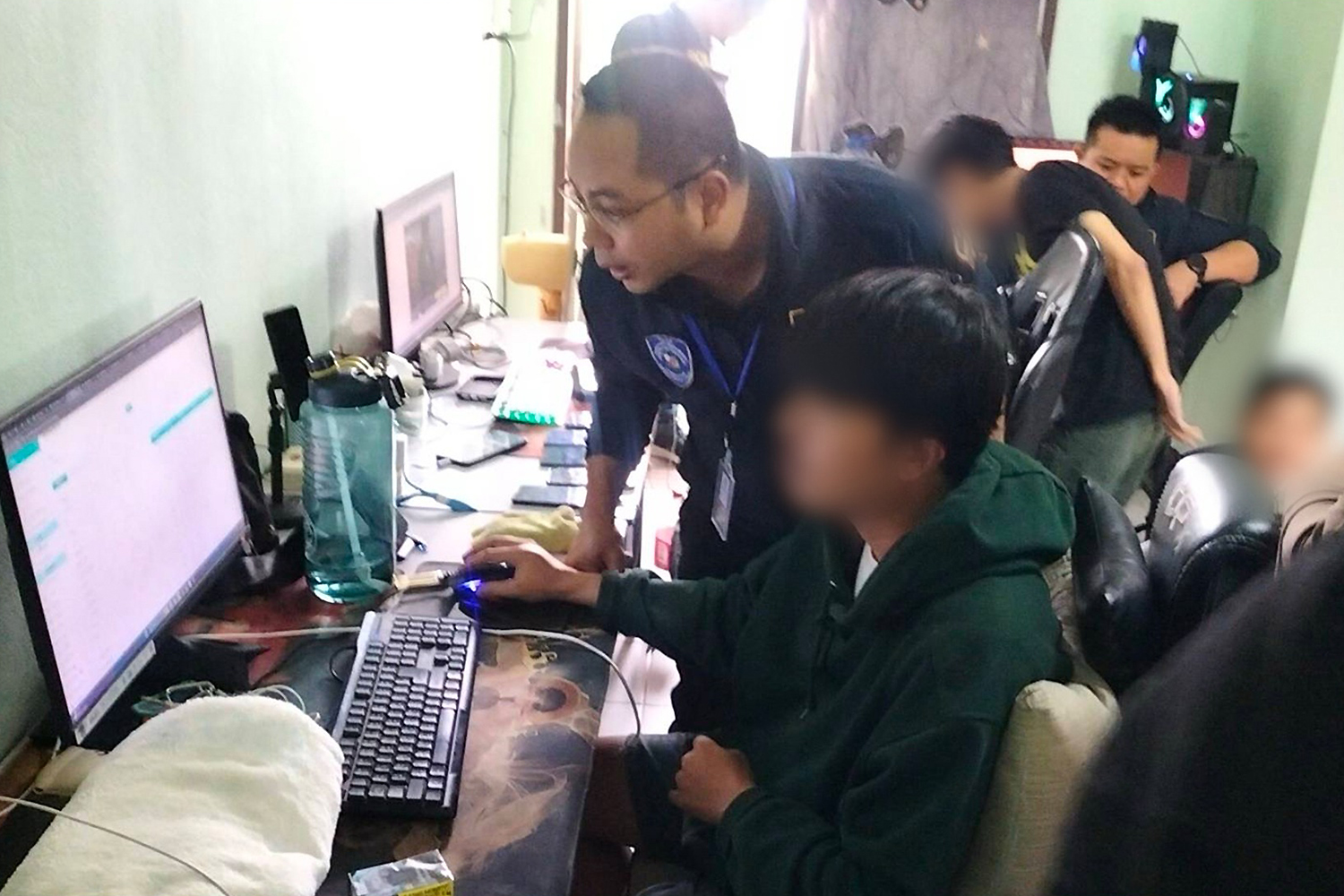 One of the suspects linked to a major online gambling network shows the website’s functions to a police officer at a residence in Hua Hin on Saturday. (Photo: CCIB)